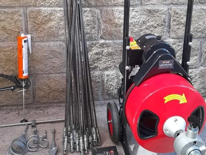 Juego de varillas flexibles de destape apoyadas en un muro junto a cabezales de distintas formas y una sonda rotatoria roja