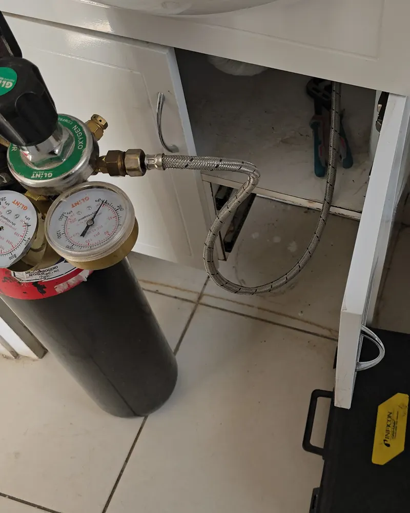 Cilindro de gas trazador con regulador y dos manómetros conectado a la red de agua junto a un WC