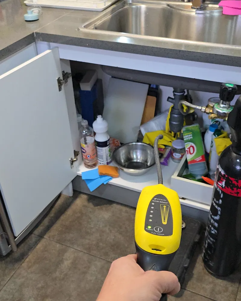 Detector de gas trazador amarillo revisando bajo el mueble abierto de un lavaplatos