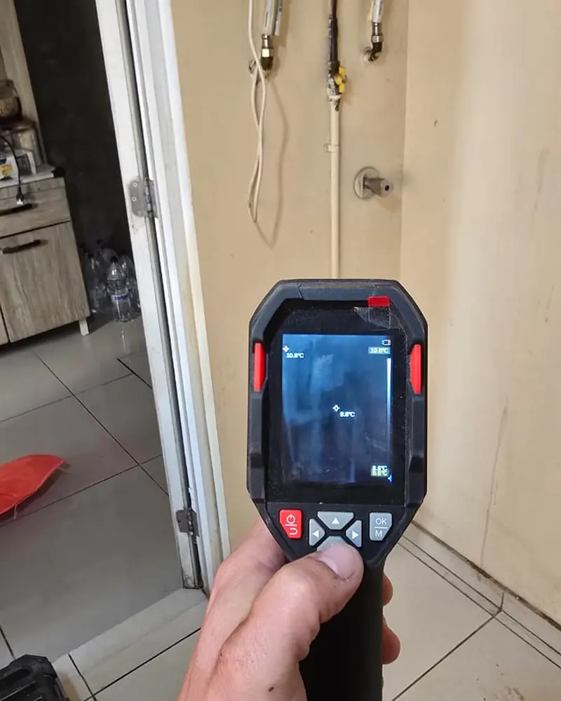 Cámara termográfica en mano apuntando al muro bajo un calefont
