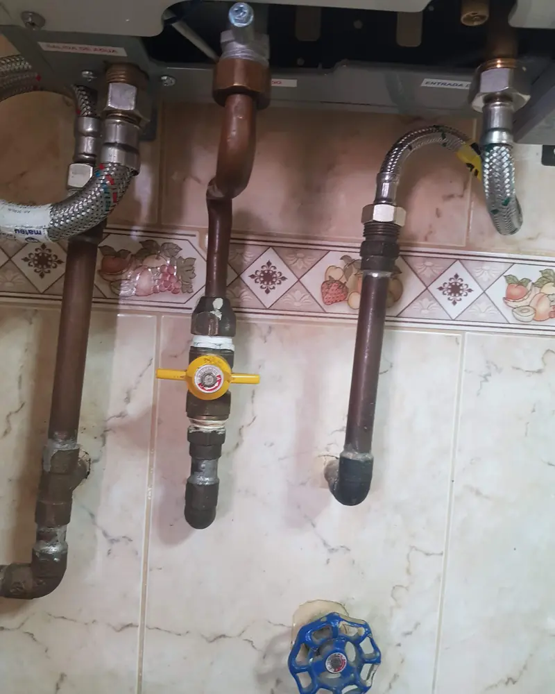 Cañerías de cobre bajo un calefont con una llave de gas amarilla
