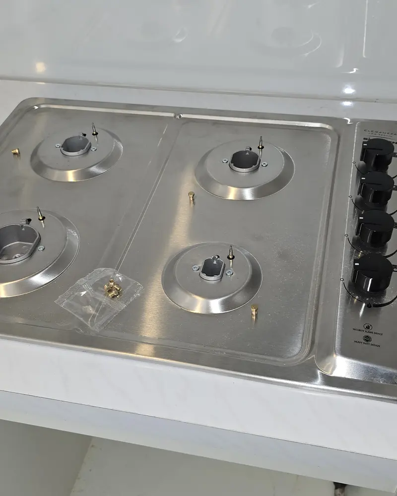 Encimera a gas de acero con cuatro quemadores sobre un mesón blanco