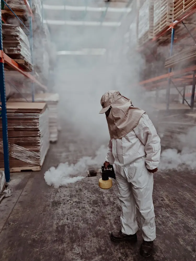 Técnico con traje de protección nebulizando el pasillo de una bodega