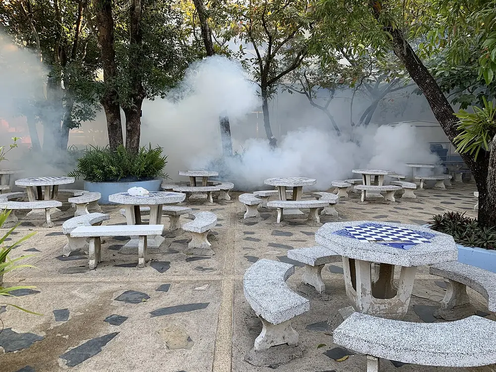 Nebulización en un patio con mesas y bancas de concreto