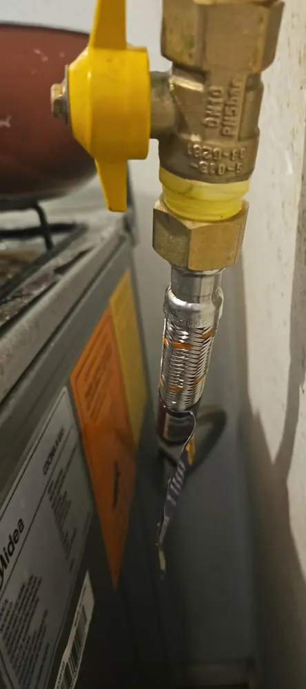 Llave de gas amarilla con flexible metálico hacia un calefont