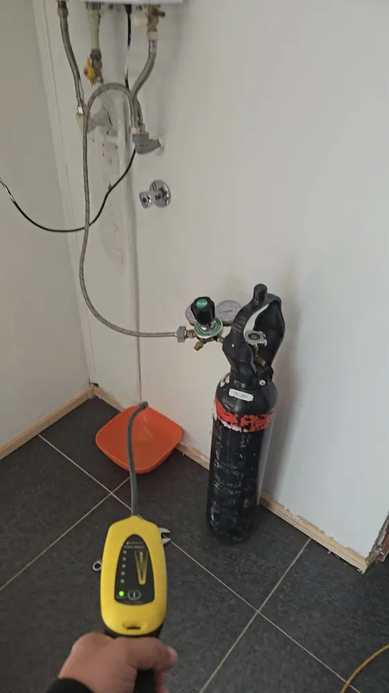 Cilindro de gas de prueba con manómetros conectado a la red de un calefont, con un detector en primer plano